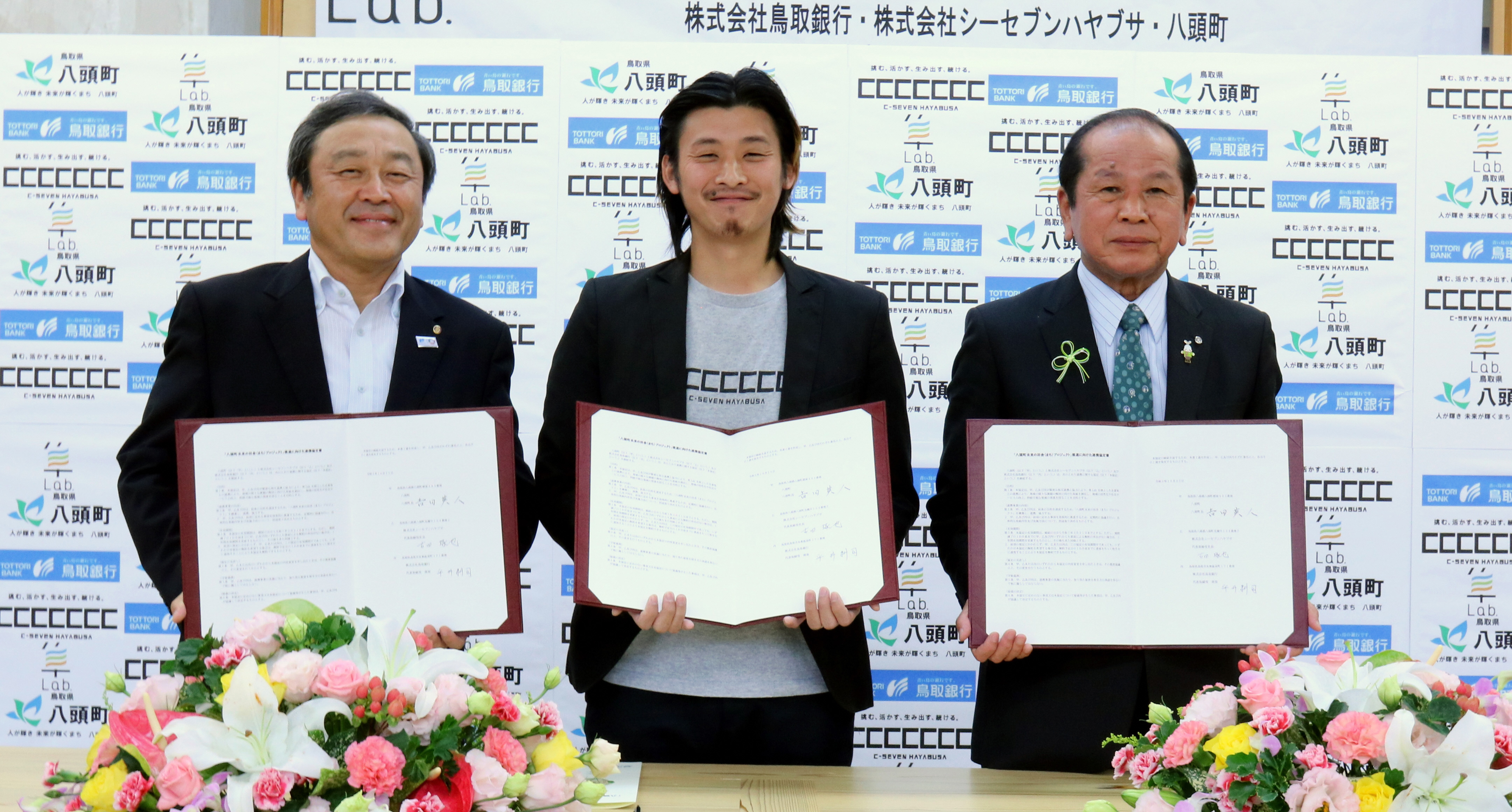 締結式で協定書を掲げる平井頭取、古田社長および吉田町長の写真