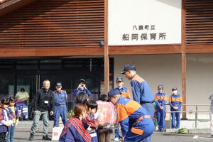 消防団副団長と八頭消防署員に贈り物を渡す園児たち