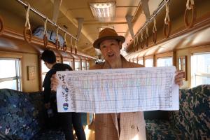 「若桜鉄道ダイヤ表手ぬぐい」を手に持つ寅さんの恰好をした商工会スタッフ