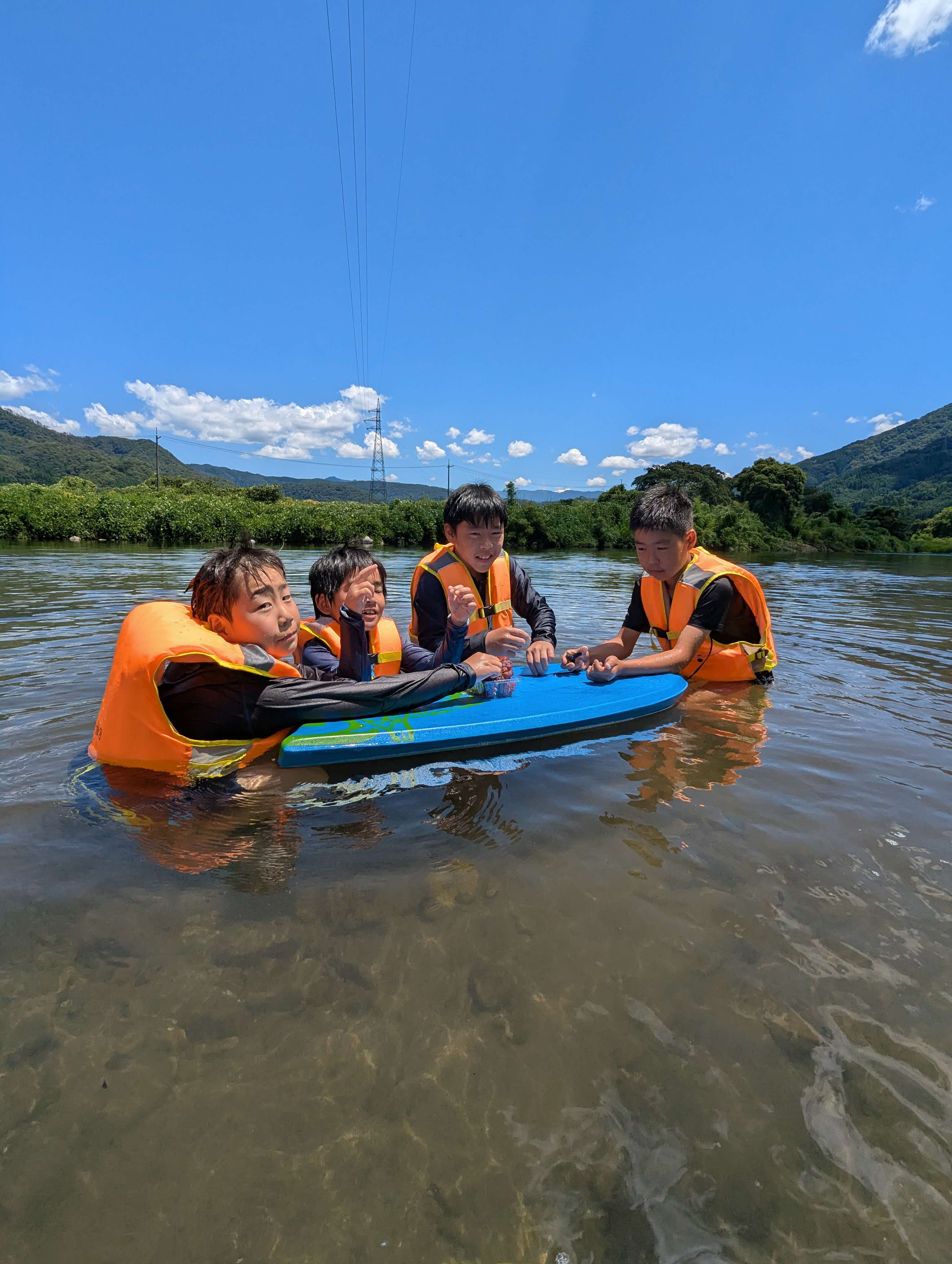 八東川遊びでビート板に浮かびながらお弁当を食べようとする男の子たち