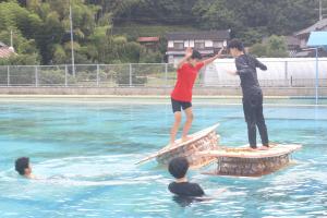 いかだの上で手押しゲームをする中学生と大学生